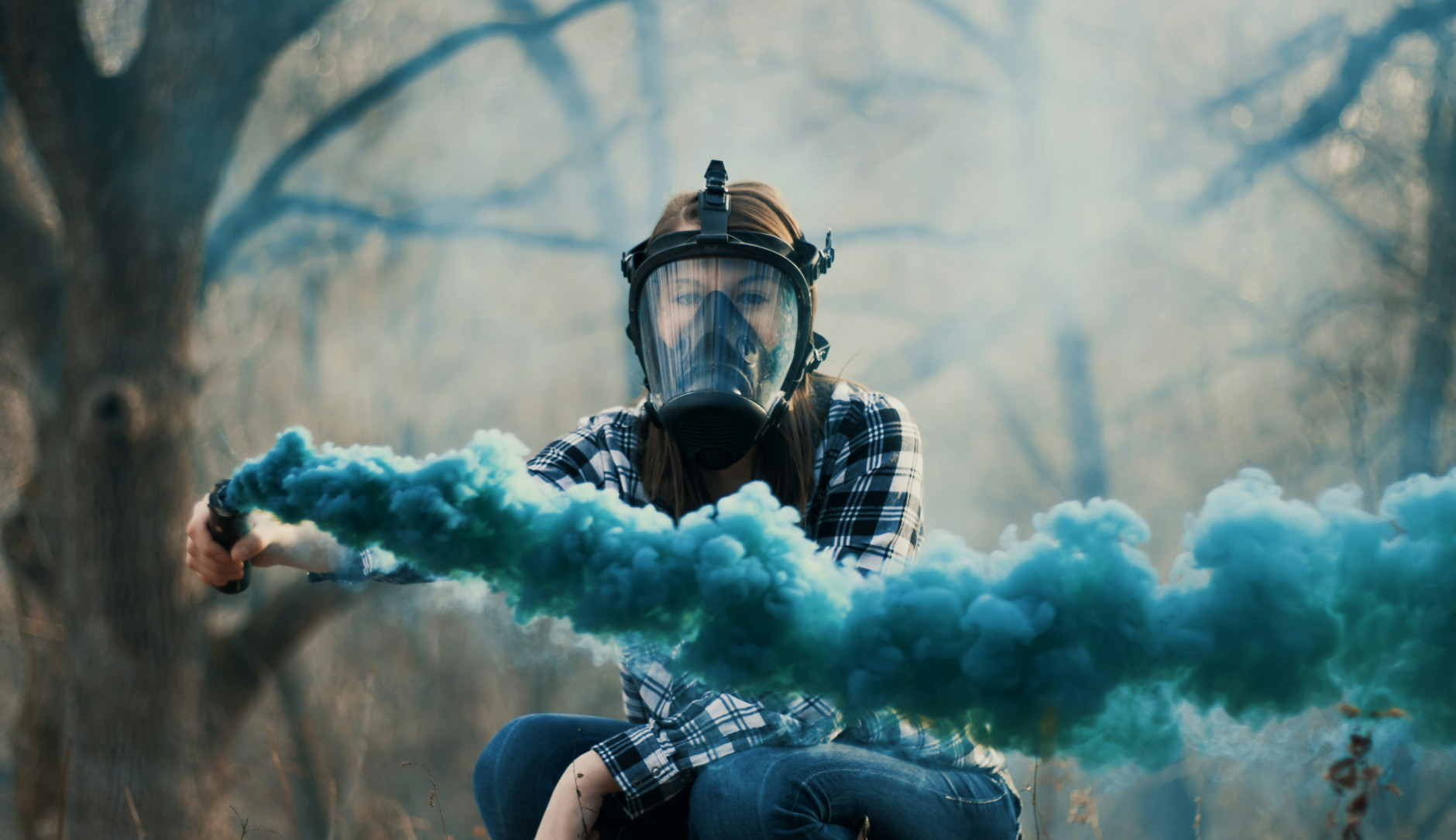 Une femme portant un masque à gaz et tenant une fusée bleue devant un fond d'arbres.