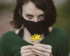 Femme avec masque tenant une petite fleur jaune