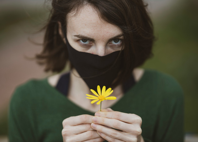 Femme avec masque tenant une petite fleur jaune