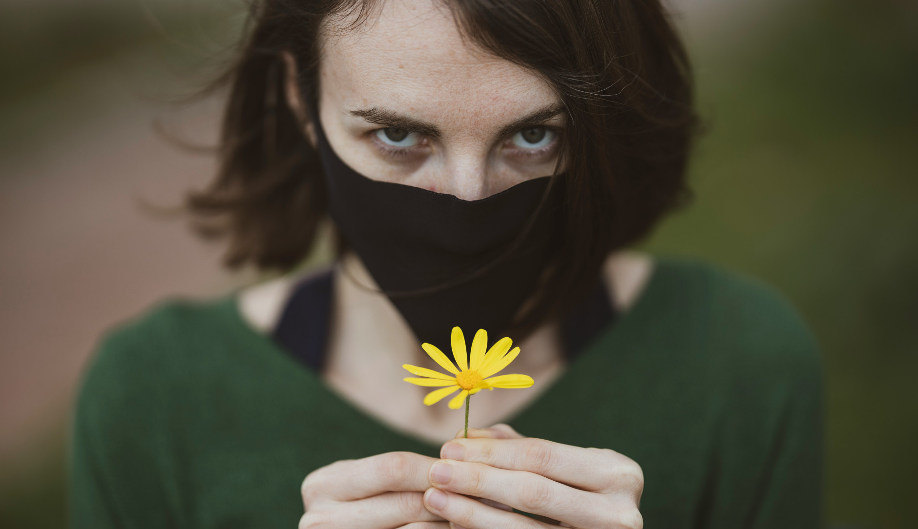 Femme avec masque tenant une petite fleur jaune