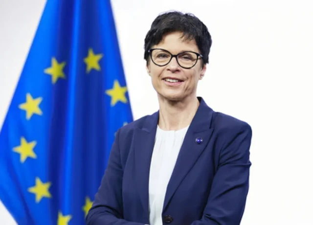 commissaire Kos devant drapeau européen