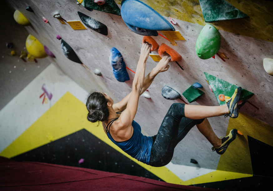 a dark haired woman working her way up a climbing wall