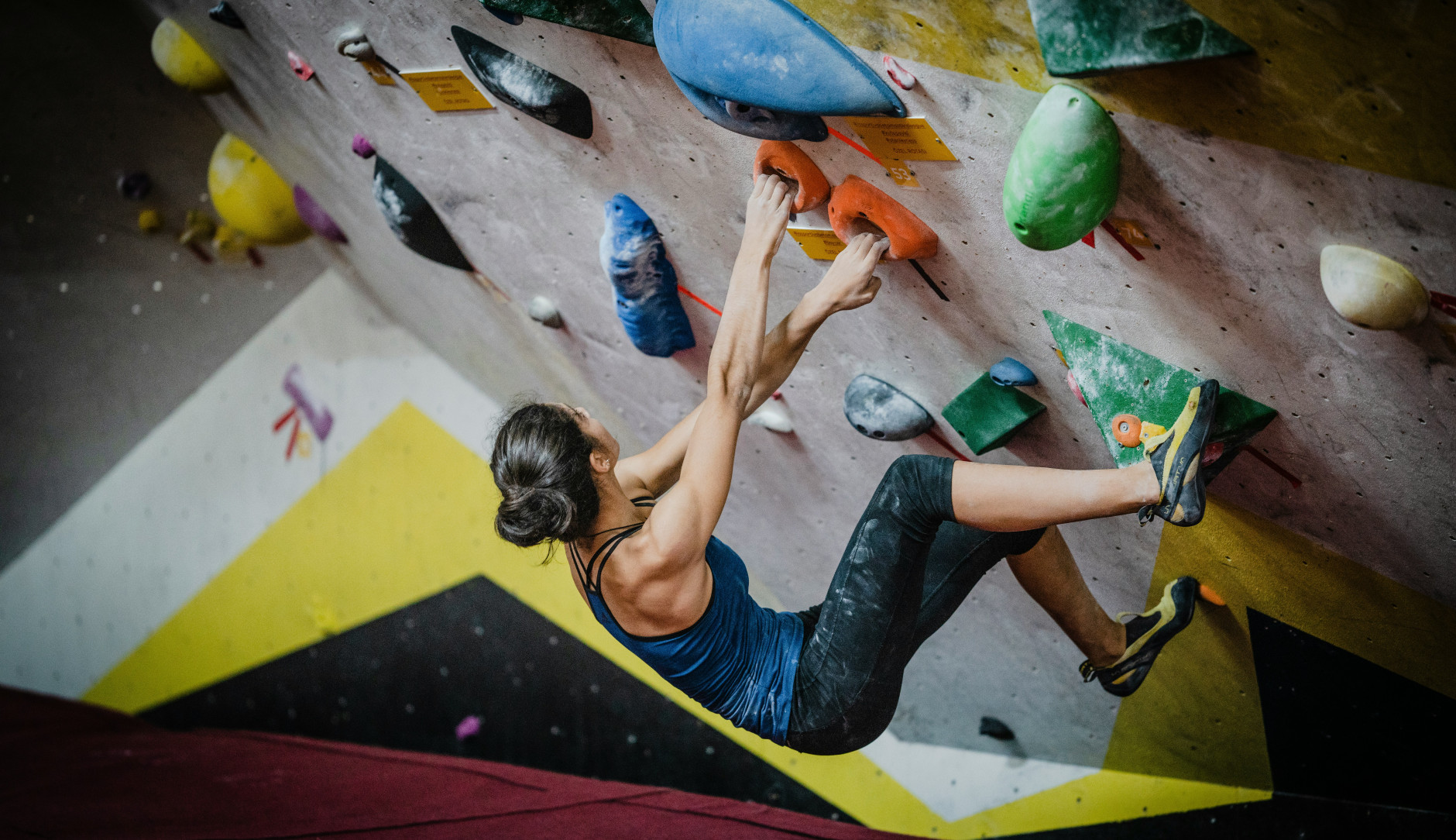 a dark haired woman working her way up a climbing wall