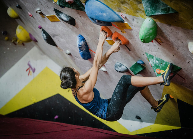 a dark haired woman working her way up a climbing wall