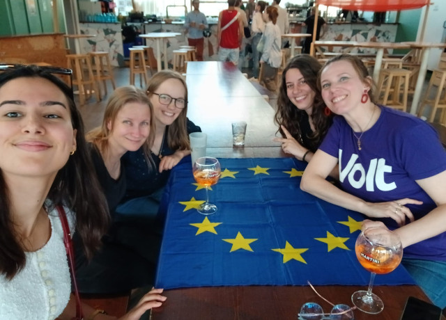 selfie 5 jeunes femmes souriantes attablées, tee shirt volt et drapeau européen