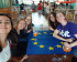 selfie 5 jeunes femmes souriantes attablées, tee shirt volt et drapeau européen