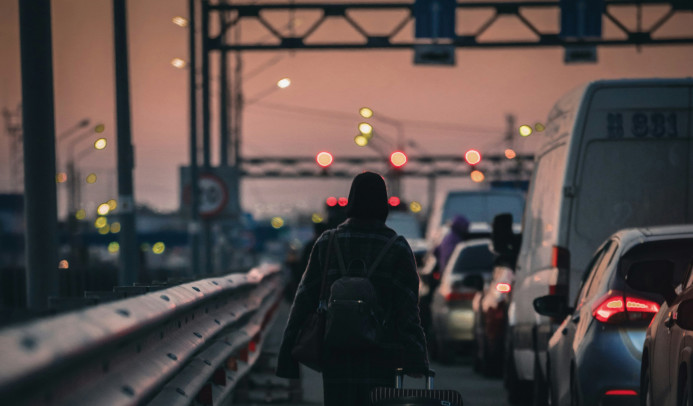 Une silhouette marchant avec une valise le long d'une route très fréquentée, vue de dos