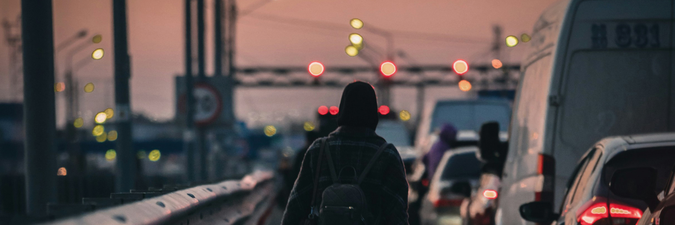 Une silhouette marchant avec une valise le long d'une route très fréquentée, vue de dos